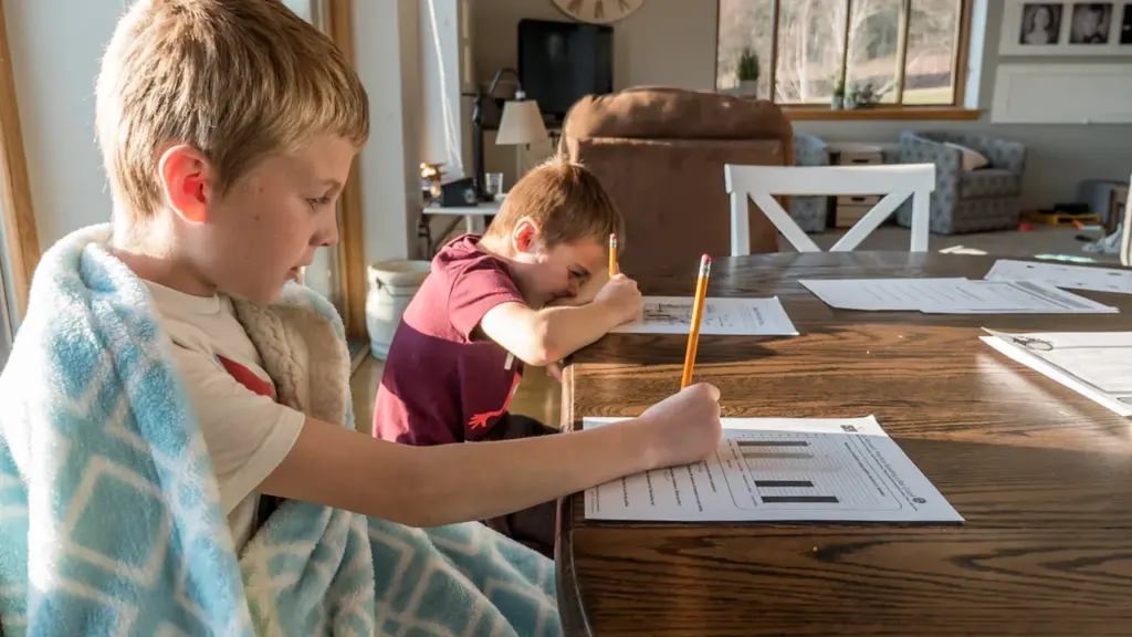 Deux jeunes enfants travaillant sur leurs devoirs scolaires à une table en bois.