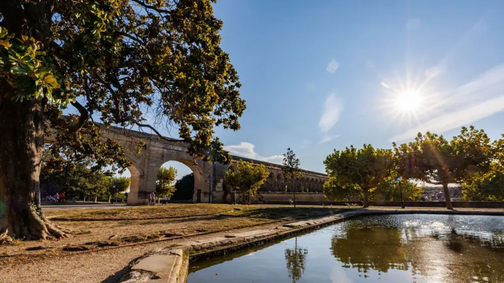 Un ancien aqueduc en pierre dominant un parc ensoleillé avec un étang au premier plan.
