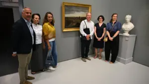 Un groupe de six personnes pose devant un tableau paysager dans une galerie d'art.