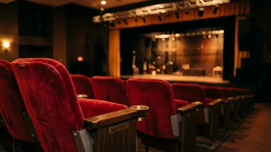 Sièges de théâtre rouges en velours faisant face à une scène sombre éclairée par projecteurs.