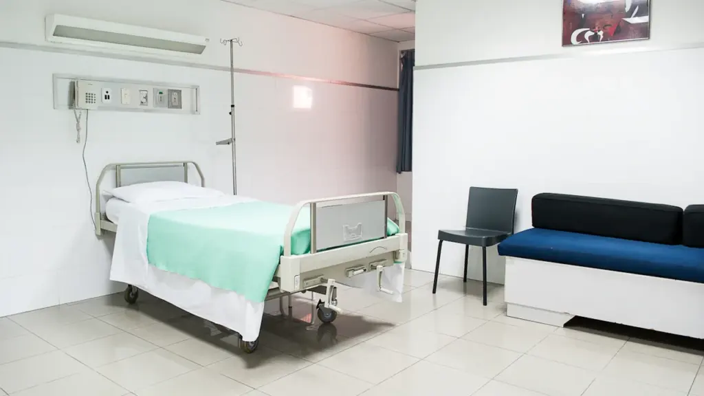 Chambre d'hôpital moderne avec lit médicalisé et banquette d'attente pour les patients.