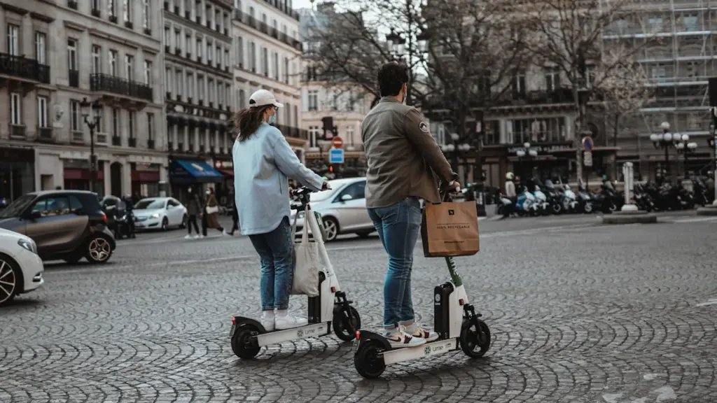 Deux personnes utilisent des trottinettes électriques sur une place urbaine à Paris.