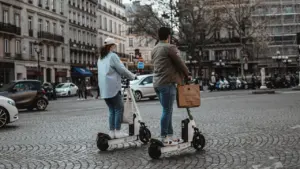 Deux personnes utilisent des trottinettes électriques sur une place urbaine à Paris.