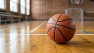 Un ballon de basket en cuir orange posé sur le parquet d'un gymnase vide.