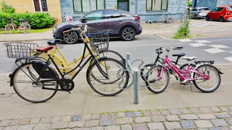 Plusieurs vélos, dont des modèles pour enfants, stationnés sur un trottoir urbain pavé.