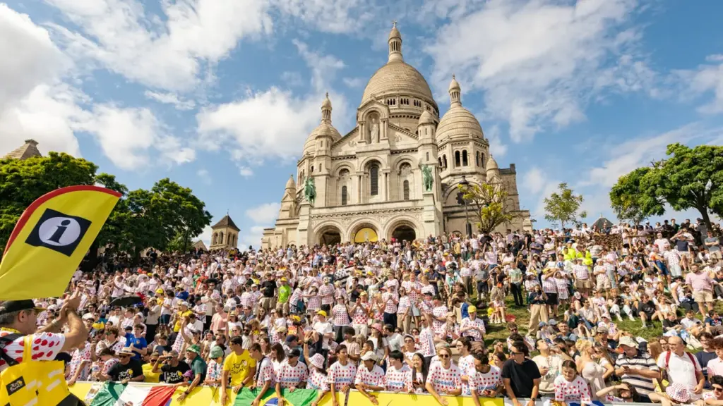 Foule joyeuse devant la basilique du Sacré-Cœur à Paris sous un ciel bleu ensoleillé.
