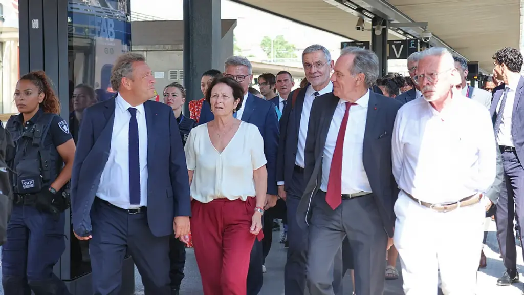 Un groupe de personnalités politiques marchant sur un quai de gare avec des agents.