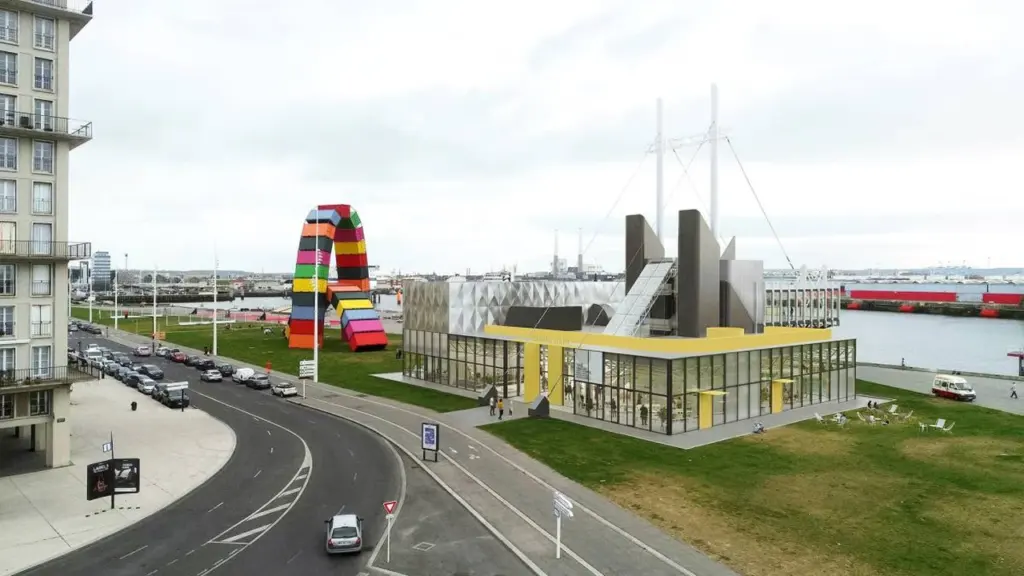 Vue aérienne d'un bâtiment moderne jaune près d'une sculpture monumentale colorée en forme d'arche.