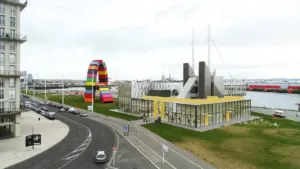 Vue aérienne d'un bâtiment moderne jaune près d'une sculpture monumentale colorée en forme d'arche.