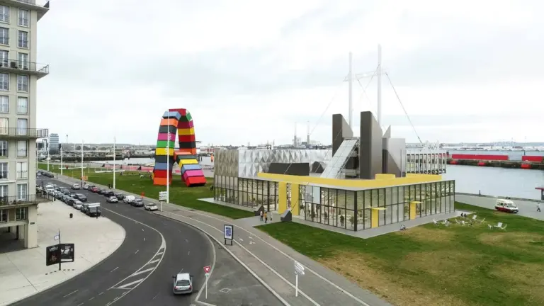 Vue aérienne d'un bâtiment moderne jaune près d'une sculpture monumentale colorée en forme d'arche.