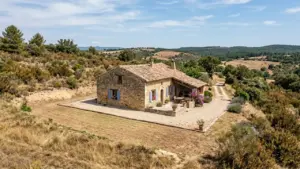 Une maison traditionnelle en pierre avec des volets bleus dans un paysage méditerranéen aride.