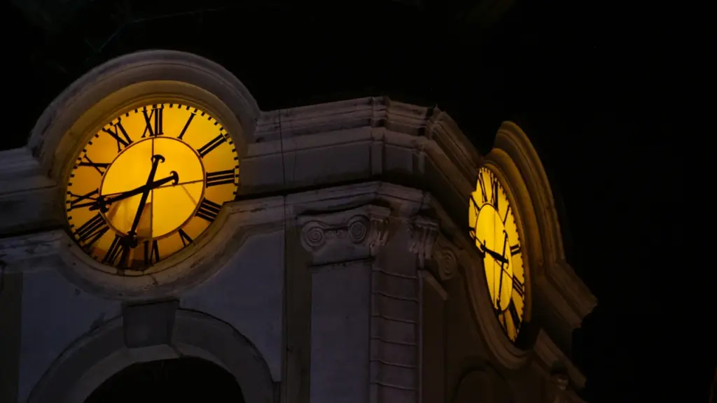 Gros plan sur une horloge de clocher ancienne illuminée durant la nuit.