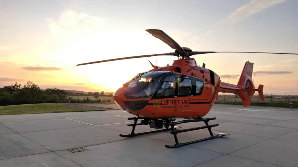 Un hélicoptère de secours orange stationné sur un tarmac au coucher du soleil.