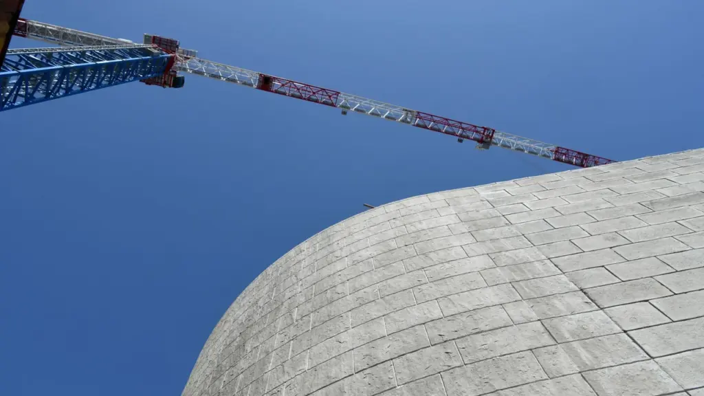 Une grue de chantier en métal domine un mur courbe en briques de béton gris.