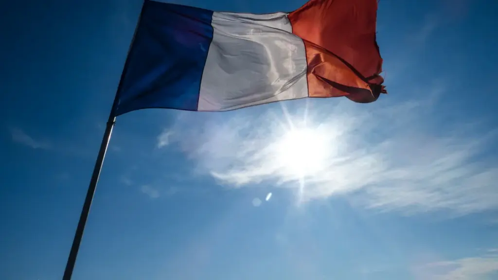 Drapeau français flottant sous un soleil intense dans un ciel bleu dégagé.