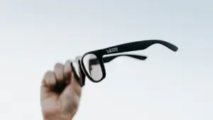 Main en l'air tenant des lunettes de vue devant le ciel clair.