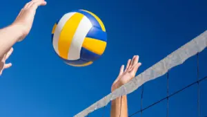 Mains de joueurs atteignant un ballon de volley-ball jaune, blanc et bleu en plein ciel.