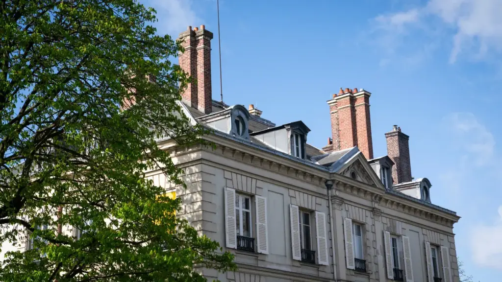 Façade d'un bâtiment classique avec des cheminées en brique sous un ciel bleu dégagé.