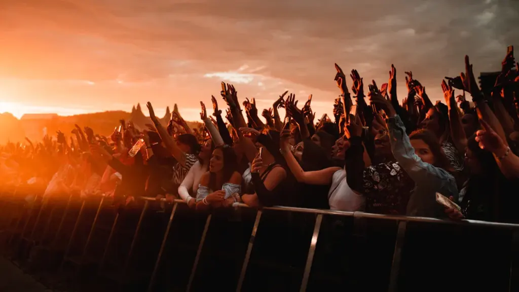 Foule en fête levant les mains lors d'un concert en plein air au coucher soleil.