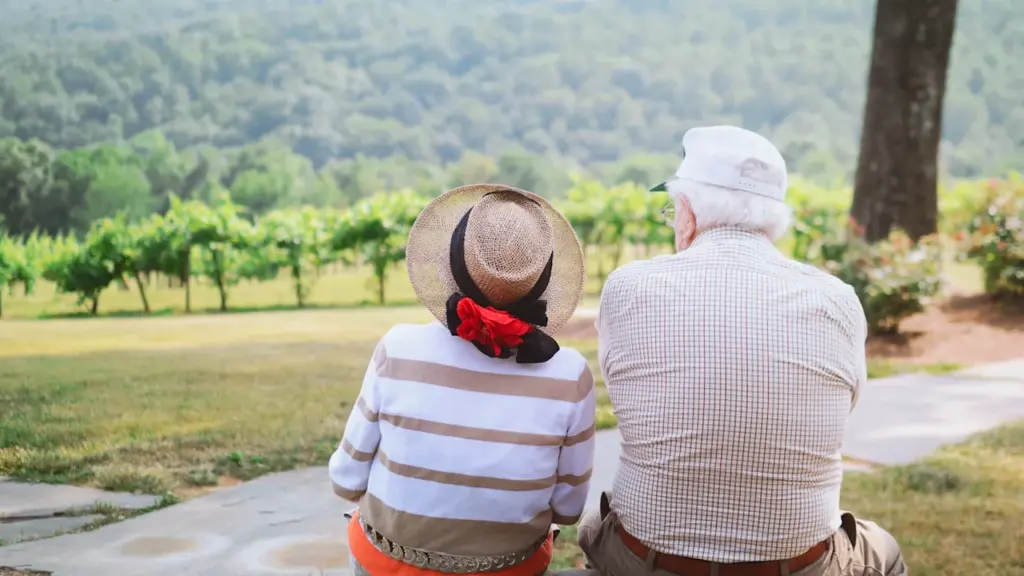 Un couple de seniors assis sur un chemin surplombant un paysage verdoyant et paisible.